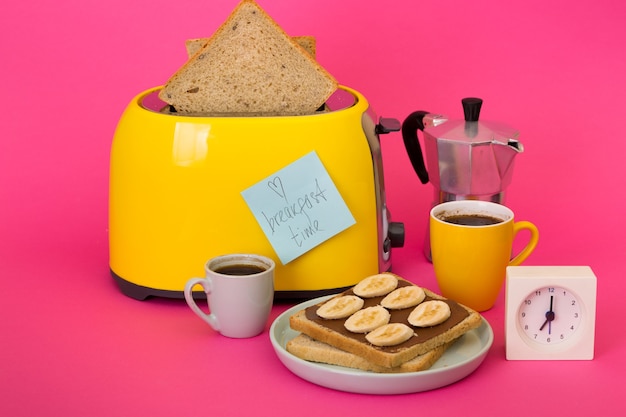 Colazione luminosa e divertente. tostapane giallo e una tazza di caffè su sfondo rosa