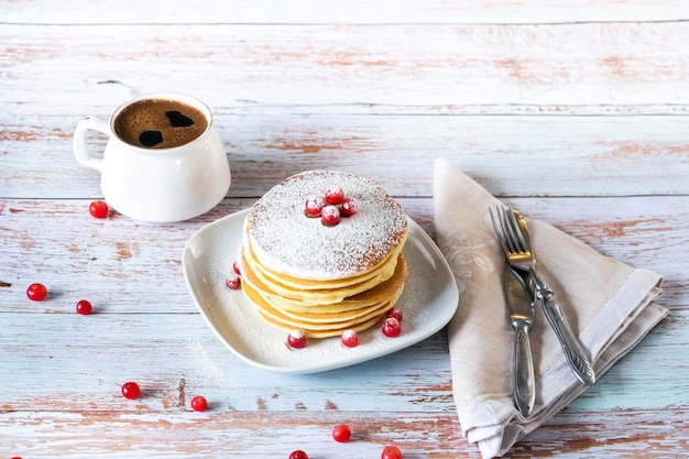 Colazione mattutina a base di pancake con mirtilli rossi e zucchero a velo su un tavolo di legno e una tazza di caffè