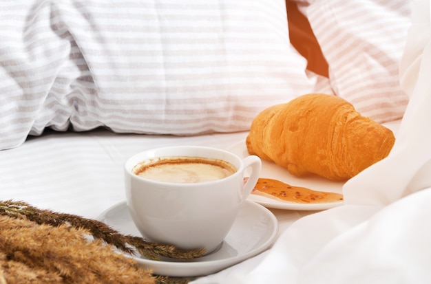 Colazione mattutina a letto. Tazza di caffè con croissant su sfondo bianco