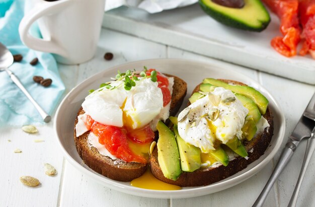 Colazione mattutina Panino bollito con uova in camicia con salmone avocado e caffè su un tavolo di legno