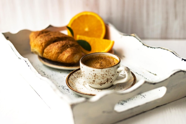 Colazione mattutina tazza di caffè sul piattino croissant frutta arancione fresca su vassoio di legno bianco shabby chic