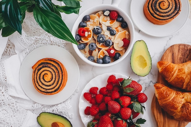 Colazione, mini pancake con fragole, croissant e avocado, delizioso cibo estivo, vista dall'alto su un retro in marmo