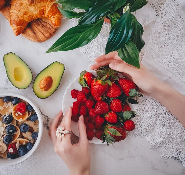 Colazione, mini pancake con fragole, croissant e avocado, delizioso cibo estivo, vista dall'alto su un retro in marmo