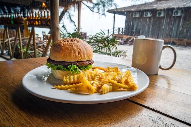 Colazione nel caffè di strada hamburger fresco e gustoso e patatine fritte sul tavolo di legno cibo nocivo dannoso per la salute