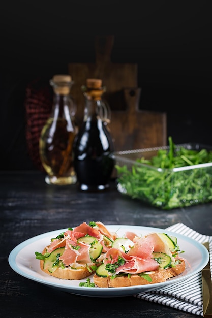 Colazione o brunch. Panino aperto con prosciutto o jamon sul piatto bianco. Antipasto mediterraneo.