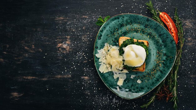 Colazione Pane tostato con spinaci Uovo in camicia e parmigiano su uno sfondo di legno nero Copia spazio