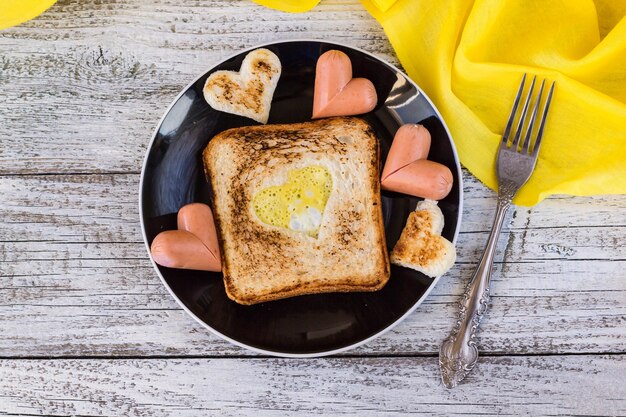 Colazione per la celebrazione di San Valentino - toast con uova strapazzate a forma di cuori, salsicce in un piatto e una forchetta