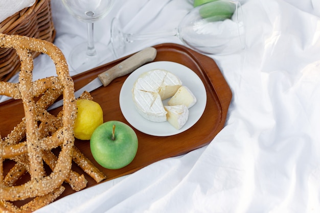 Colazione picnic all'alba, sul lenzuolo bianco d'erba con vassoio con formaggio e vite, pane secco, mela, limone. umore romantico, concetto estetico di stile di vita lento, vista dall'alto