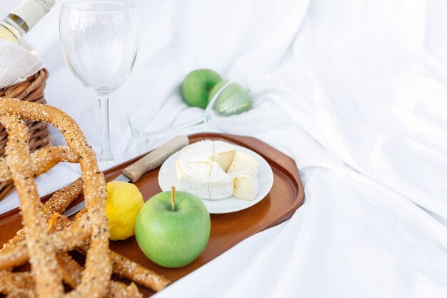 Colazione picnic all'alba, sul lenzuolo bianco d'erba con vassoio con formaggio e vite, pane secco, mela, limone. umore romantico, concetto estetico di stile di vita lento, vista dall'alto