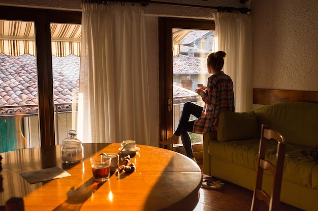 Colazione - ragazza seduta sul divano con una tazza di caffè e guardando fuori dalla finestra