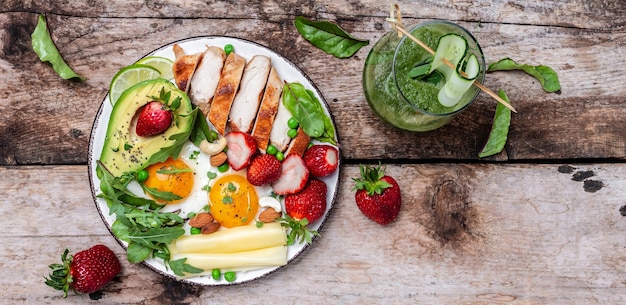 Colazione ricca di grassi a basso contenuto di carboidrati, filetto di pollo alla griglia e avocado, uova fritte con fragole, formaggio e noci. Frullato detox, verde fresco, dieta chetogenica. Concetto di cibo sano, vista dall'alto,