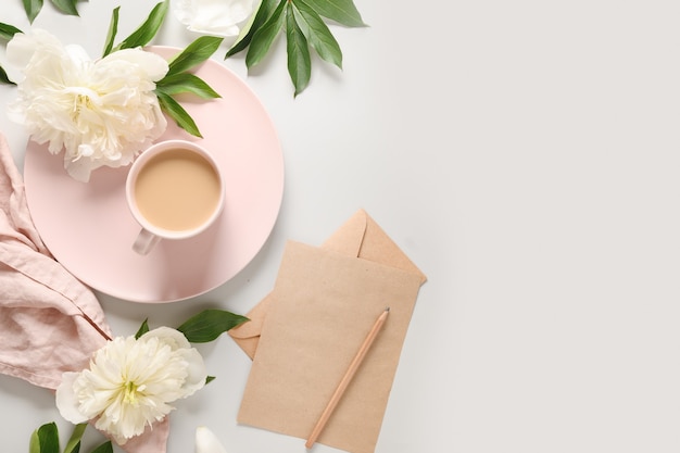 Colazione romantica estiva con tazza di caffè e fiori di peonie bianche sulla scrivania grigia dell'ufficio