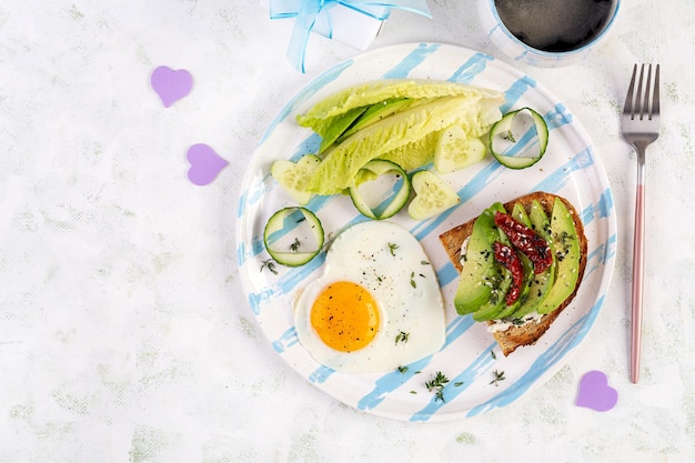 Colazione romantica per San Valentino Uovo fritto e pane tostato con avocado e crema di formaggio Vista dall'alto