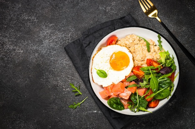 Colazione salata Porrige di farina d'avena con uovo di salmone salato e insalata fresca Vista dall'alto sul tavolo nero