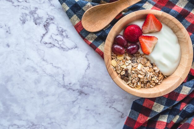 Colazione salutare. Ciotola di muesli fatti in casa con yogurt e frutta fresca sul tavolo di marmo.