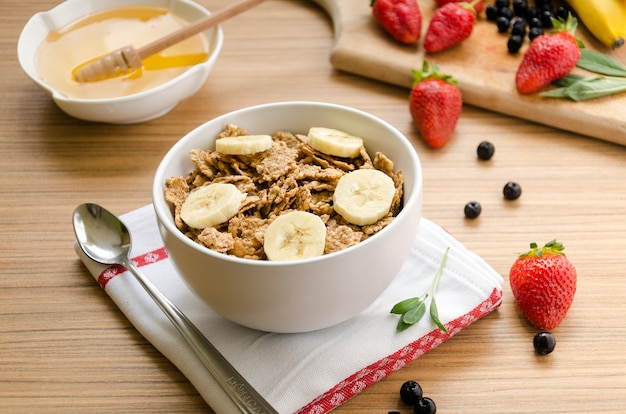 Colazione salutare con una ciotola di cereali (muesli), fragole, frutti di bosco, miele e banan