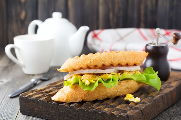 Colazione salutare. Panino farcito con uova strapazzate, prosciutto e foglie di lattuga su fondo in legno vecchio. Messa a fuoco selettiva.