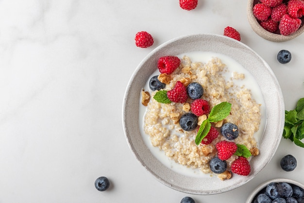 Colazione salutare. Porridge di quinoa con frutti di bosco freschi, noci e menta in una ciotola su sfondo bianco. vista dall'alto con copia spazio