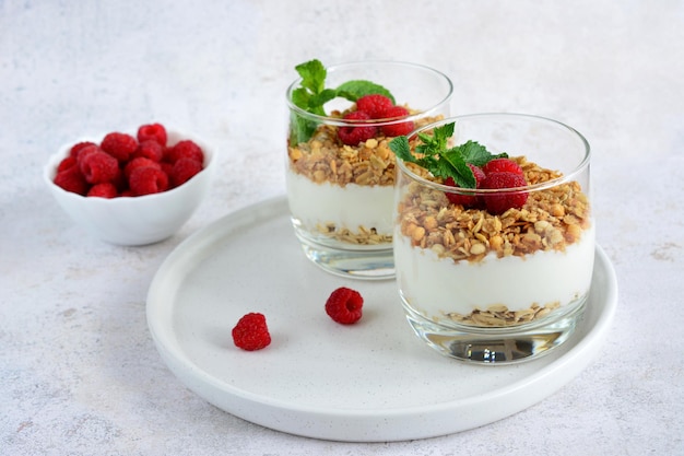 colazione sana con yogurt, muesli e lampone in vetro su vassoio bianco, primo piano