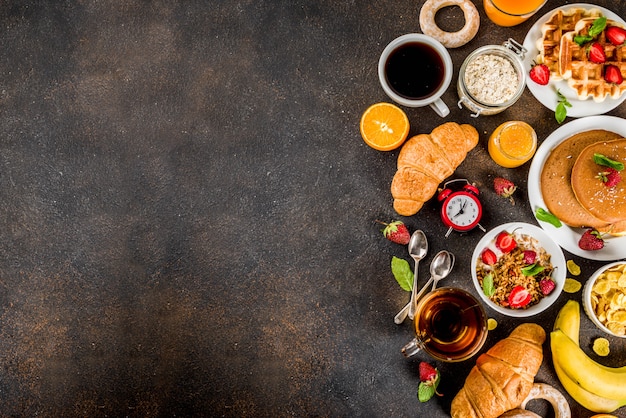 Colazione sana mangiare concetto, vari cibi mattutini - frittelle, cialde, cornetti sandwich di farina d'avena e muesli con yogurt, frutta, bacche, caffè, tè, succo d'arancia