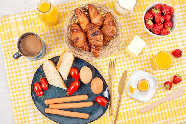 Colazione servita con caffè, cornetti, salsicce, uova, frutti di bosco freschi, latte, burro, succo d'arancia