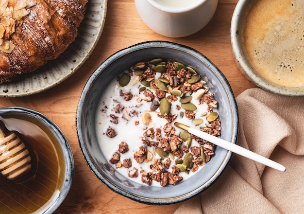 Colazione su un tavolo di legno: muesli, cornetto, caffè e latte,