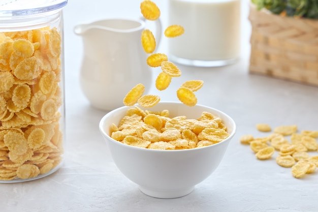 Colazione tradizionale con fiocchi di mais che cadono in una ciotola con latte su un tavolo bianco