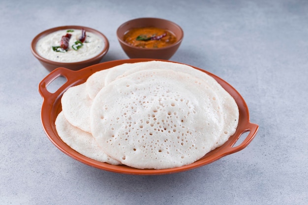 Colazione tradizionale dell'India meridionale Dosa o Thattu dosa realizzata con ghisa dosa thawa disposti in stoviglie con contorno chutney di cocco bianco e chutney di cipolla su sfondo bianco testurizzato