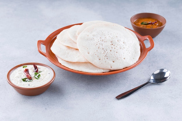 Colazione tradizionale dell'India meridionale Dosa o Thattu dosa realizzata con ghisa dosa thawa disposti in stoviglie con contorno chutney di cocco bianco e chutney di cipolla su sfondo bianco testurizzato
