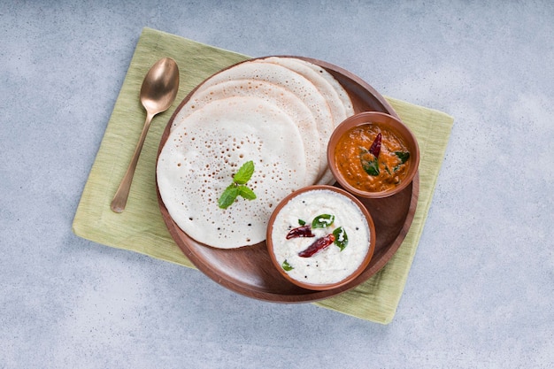 Colazione tradizionale dell'India meridionale Dosa o Thattu dosa realizzata con ghisa dosa thawa disposti in stoviglie con contorno chutney di cocco bianco e chutney di cipolla su sfondo bianco testurizzato