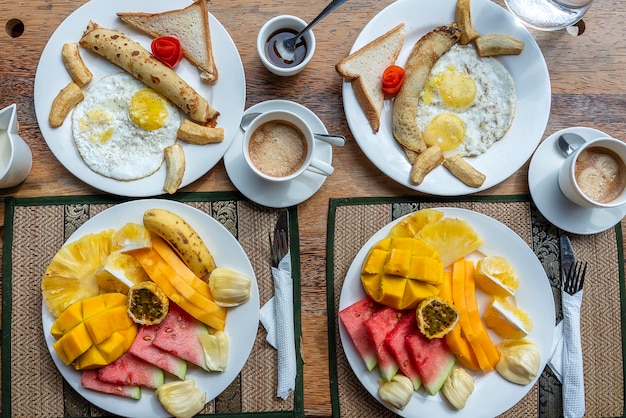 Colazione tropicale a base di caffè alla frutta e uova strapazzate e pancake alla banana per due sulla spiaggia vicino al mare