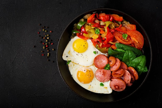 Colazione. Uova fritte con salsiccia e verdure in una padella su uno sfondo nero