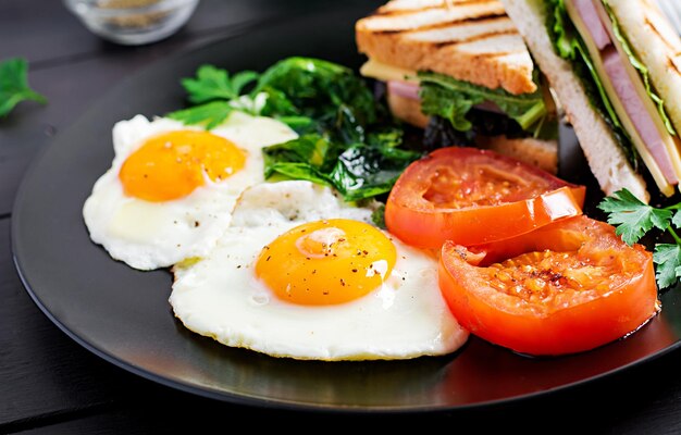 Colazione uova fritte spinaci pomodori e club sandwich sul piatto