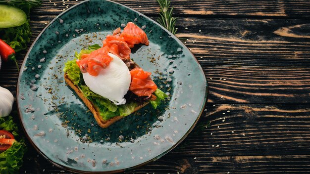 Colazione. Uovo in camicia, salmone su lattuga su crostini di pane. Su uno sfondo di legno nero. Copia spazio.