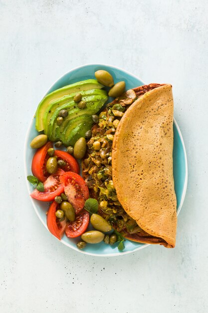 Colazione vegana di frittata di ceci senza uova e senza glutine con funghi fritti e porro. e un'insalata di pomodori freschi maturi, avocado, olive e capperi.