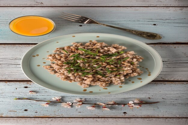 Colazione vegetariana Porridge di orzo bollito con erbe e un bicchiere di succo d'arancia su un tavolo di legno chiaro.