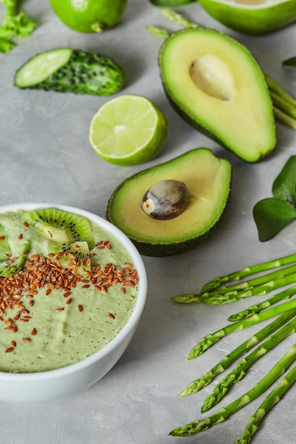 Colazione verde detox frullato ciotola condita con cetriolo, avocado, asparagi, lime e semi di lino su sfondo grigio cemento ardesia