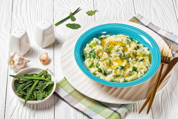 Colcannon irlandese tradizionale purè di patate con cavolo riccio, aglio, burro fuso e cipollotto servito su una ciotola blu, contropiatto bianco su uno sfondo di legno bianco, vista dall'alto, primo piano