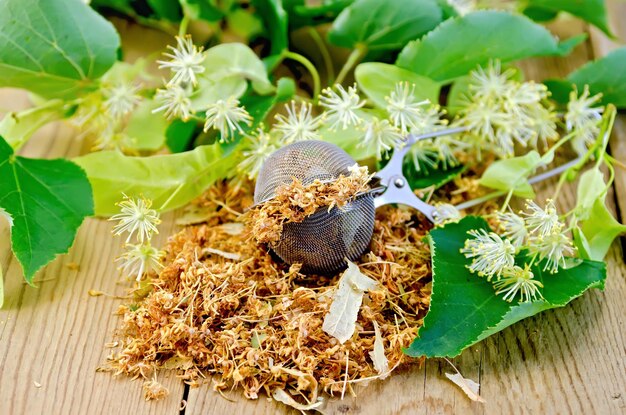 Colino in metallo con fiori secchi di tiglio, fiori di tiglio freschi su uno sfondo di assi di legno