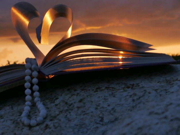 Collana di perle a forma di cuore pagine di libro piegate durante il tramonto