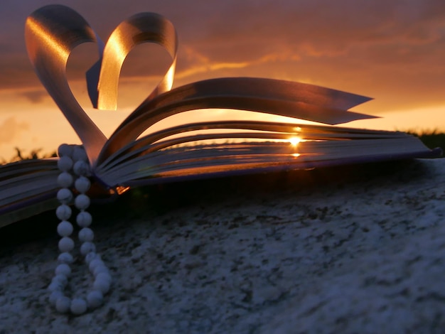 Collana di perle a forma di cuore pagine di libro piegate durante il tramonto