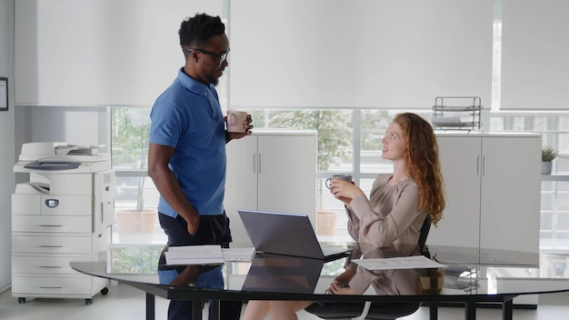 Collega multietnico maschio e femmina che discute alla scrivania guardando il computer portatile e bevendo caffè