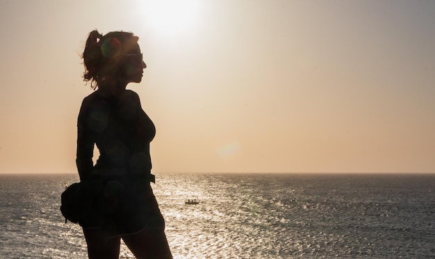 Collegamento costiero Posa della donna sulla spiaggia che abbraccia il tramonto con i pescatori di passaggio sullo sfondo