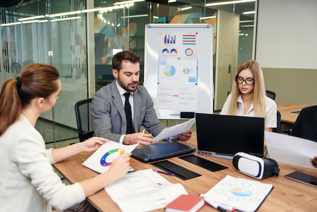 Colleghe di razza mista analizzando diversi documenti aziendali e lavorando con i computer ai tavoli in ufficio moderno.