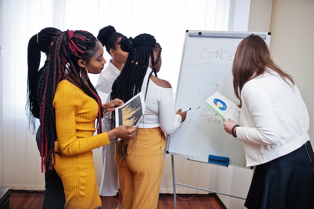 Colleghe multirazziali, troupe di diverity partner femminili in ufficio in piedi vicino a lavagna a fogli mobili.