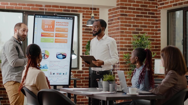 Colleghi che discutono della presentazione aziendale con analisi sul monitor nell'ufficio della società di avvio. Progetto di pianificazione delle persone e strategia di marketing, incontro con i colleghi nella sala del consiglio.