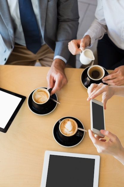 Colleghi che hanno una tazza di caffè mentre usando il telefono cellulare e la compressa digitale