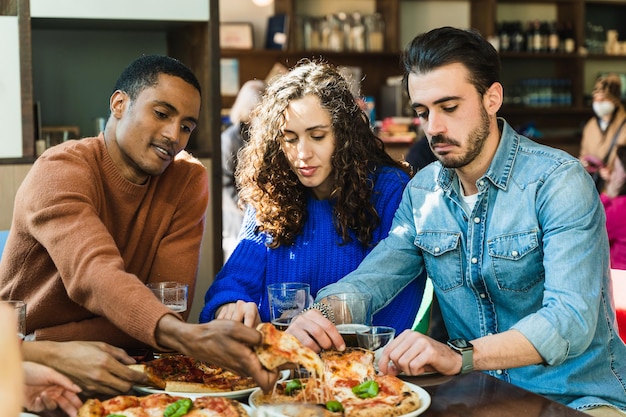 Colleghi che mangiano pizza insieme in un bar Un ragazzo africano prende una fetta di pizza