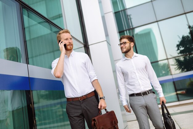 Colleghi di lavoro in camicia che camminano all'aperto e utilizzano dispositivi