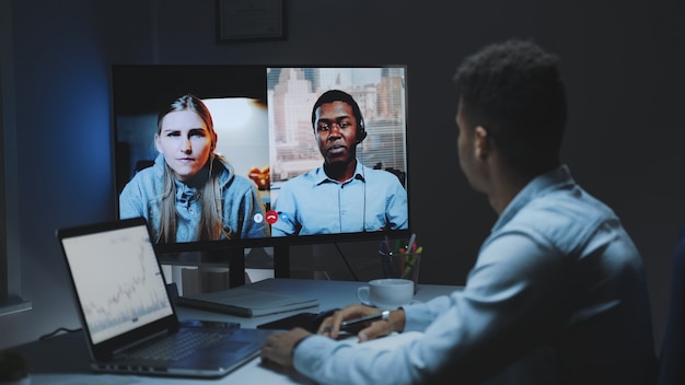 Colleghi di razza mista che lavorano a casa durante la quarantena effettuando una videochiamata comune su un grande monitor